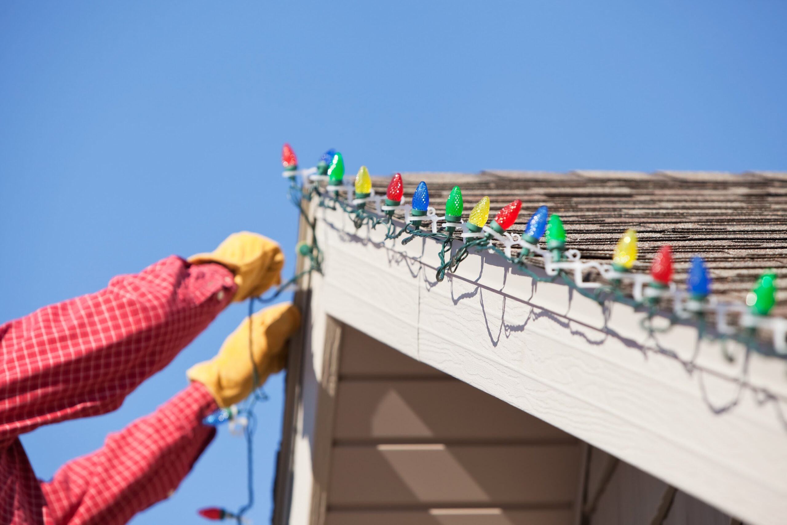 Homeowner installing outdoor Christmas lights near roofline safely